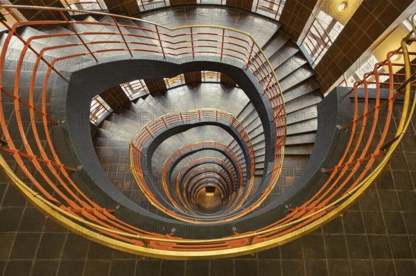 Detailed spiral staircase with orange-coloured banister and tiled floor, fascinating and artistic,