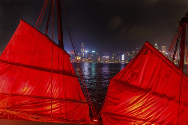 Close up of red-sail junk boat with Hong Kong island skyline background seen from the waterfront of
