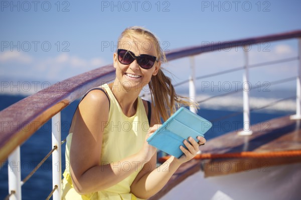 Young smiling woman in sunglasses holding tablet computer and looking somewhere while traveling by