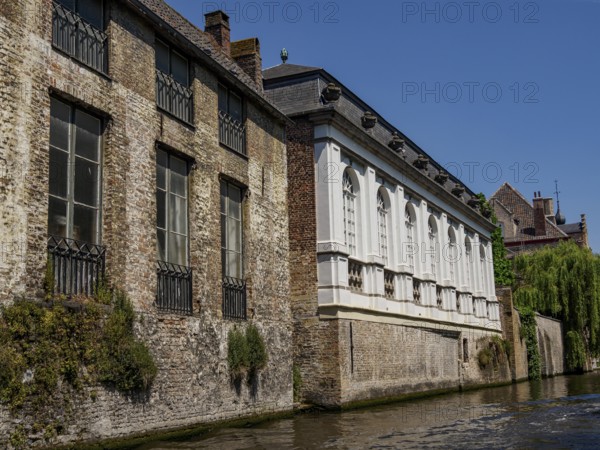 Historic buildings with brick façade along a canal, partly surrounded by greenery, under a clear