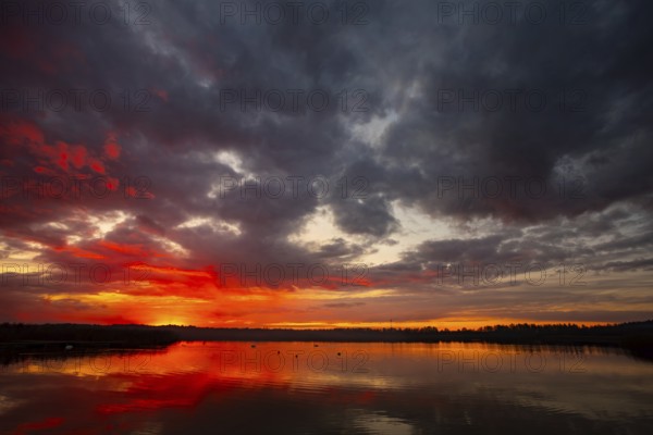 A truly stunning sunset over a calm and reflective lake showcases vibrant hues and dynamic clouds