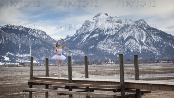 Ballerina dances elegantly on a wooden footbridge in front of snow-covered mountains, in the
