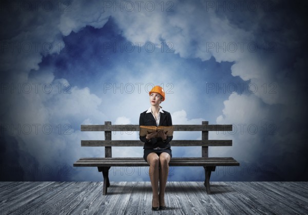 Beautiful woman architect sitting on wooden bench. Young technician specialist in orange safety