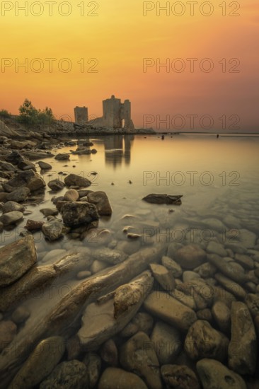 Castle ruins at dawn. Bay on the Mediterranean Sea with calm water at sunrise. Reflection of the