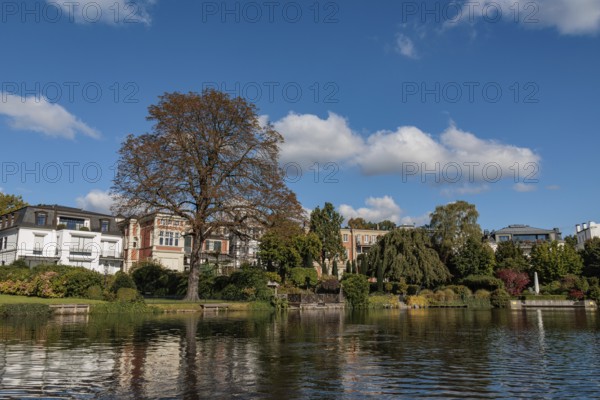 Stylish townhouses reflected in the water, surrounded by lush autumn foliage, Alster, Hamburg,