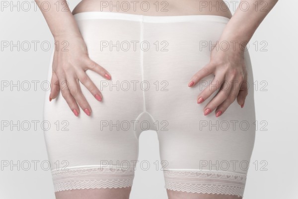 Woman's hips in pantaloons panties, back view of woman with her palms placed on her buttocks.