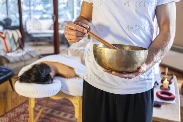 Man holding a bronze sound bowl with a stick, used for sound therapy and sound massages. A