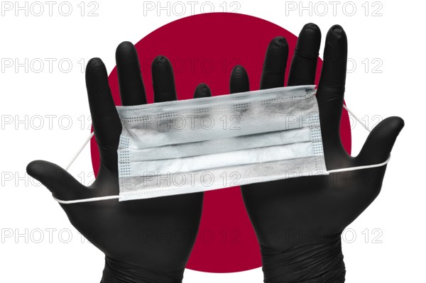 Doctor holds face mask in hands in black medical gloves on background colors flag of flag of Japan