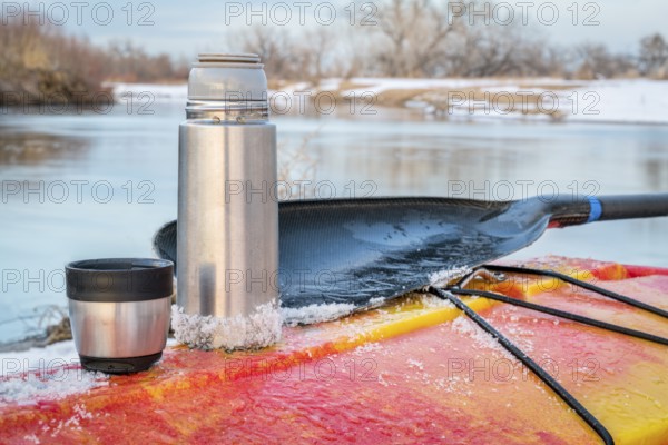 Winter kayaking in Colorado - thermos bottle with hot tea on the icy deck of a red whitewater kayak