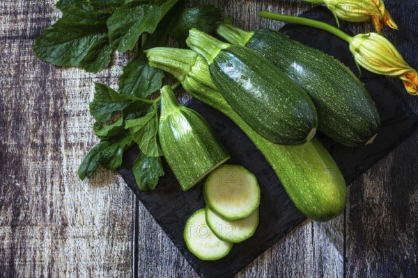Harvesting zucchini. Healthy uncooked fresh green zucchini with slice on a wooden kitchen table.