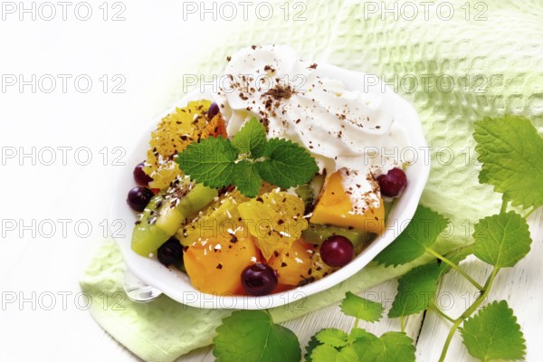 Fruit salad with orange, kiwi, cranberries and baked pumpkin, whipped cream, sprinkled with