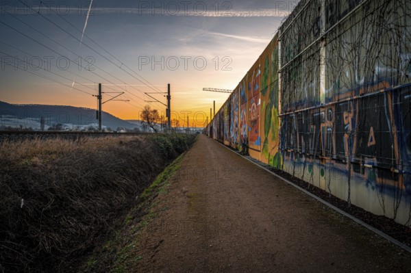 A path along a graffiti-covered wall at sunset, with rails and urban atmosphere, Jena, Thuringia,