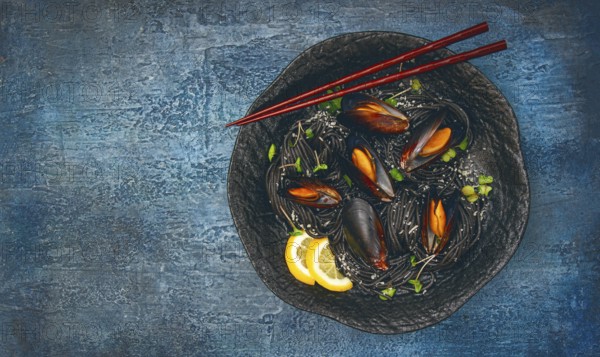 Spaghetti with black squid, black pasta, with boiled mussels, on a black plate, with parsley and