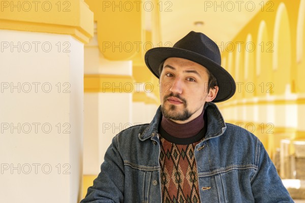 Portrait of a stylish handsome young man with a scarf outdoors. A serious man wearing a hat and a