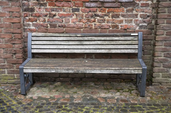 Empty wooden bench with metal frame sits against a weathered brick wall, inviting contemplation and