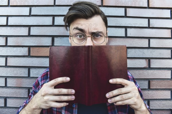 Funny face. Young hipster guy wearing eyeglasses with picked up one browe looking at camera and