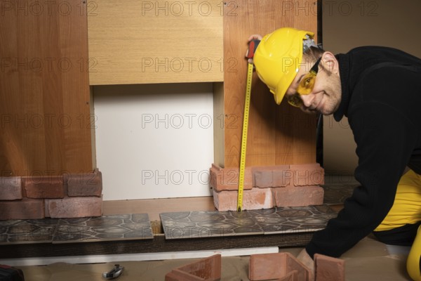 The construction worker looks at the camera and smiles while measuring. Wearing personal protective