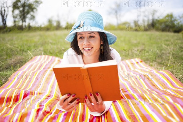 Attractive smiling young woman dressed casually reads orange old book lying down on a colourful
