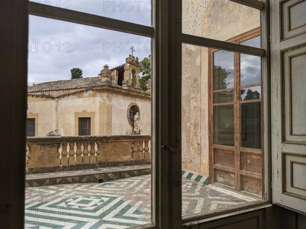 A window view of a historic terrace with patterned floor tiles and vintage architectural elements,