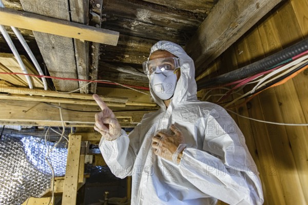 An indoor environmental quality assessor is viewed up-close, working beneath timber floor joists