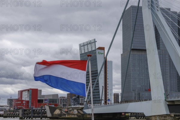 Dutch flag waving in front of a bridge and modern buildings under a cloudy sky, Rotterdam,