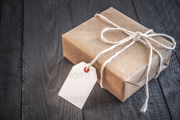 Gift box, wrapped in brown vintage paper and tied with white flax string, on an old black wooden