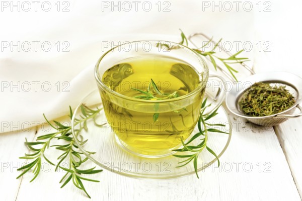 Rosemary herbal tea in a cup, a strainer with dry herb and a linen napkin on the background of a