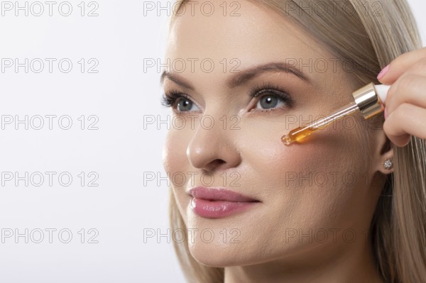A woman gently applies a brightening serum to her face, promoting radiant and healthy skin with