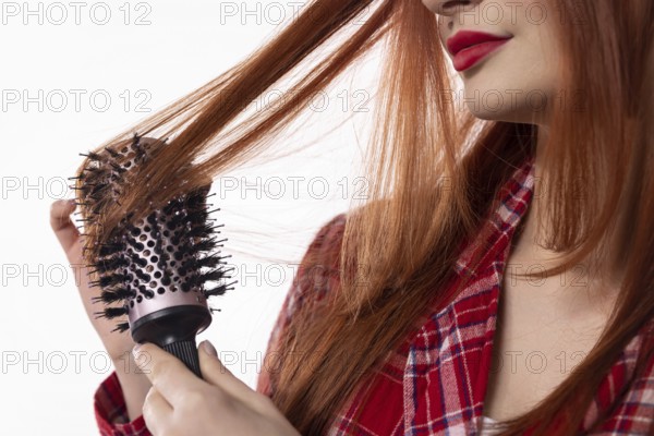 A woman is lovingly brushing her long, shiny hair with a round brush, showcasing her detailed