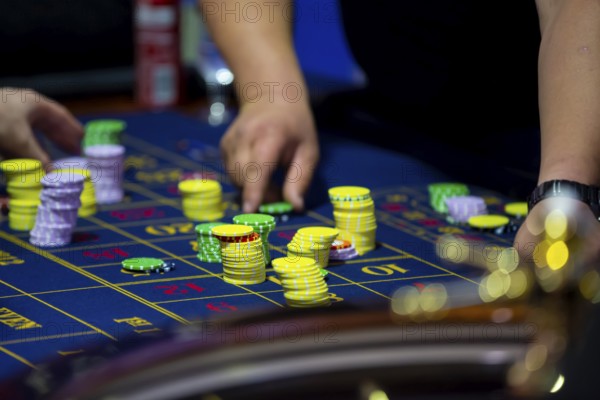 Roulette table with human hands putting down chips in casino. Roulette wheel in the foreground.