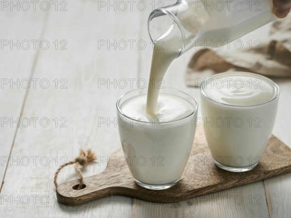 Pouring homemade kefir, buttermilk or yogurt with probiotics. Yogurt flowing from glass bottle on
