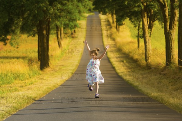 A little girl in a summer dress runs along a street in the light of a summer evening, jumping and