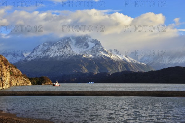 Gray lake and snow-capped mountains. By the banks of the red tourist ship sails. Summer sunset