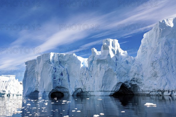 Ice formations with caves and reflections in the water under a blue sky, icebergs in the Southern