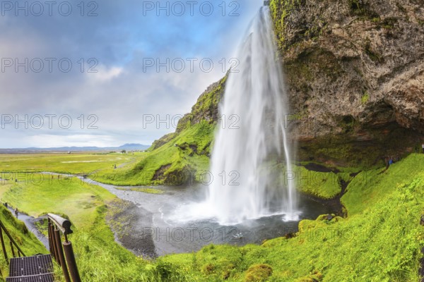 Seljalandsfoss waterfall in July. Large rainbow decorates a drop of water. The warm July day in