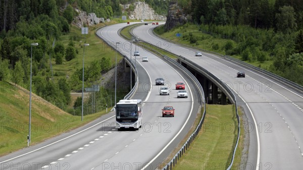 Summer motorway landscape with white Iveco Evadys tour bus among car traffic. Salo, Finland, June