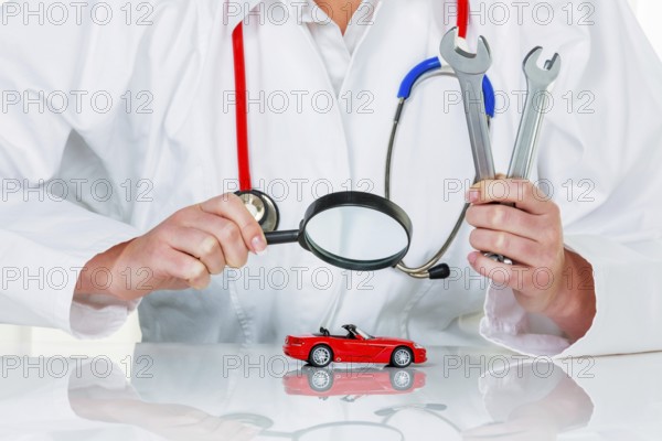 A model of a car is examined by a doctor. Symbol photo for workshop, service and car purchase.