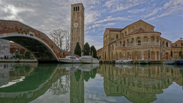Scenic canal with boats reflecting a historic church and tall bell tower under a cloudy sky, Ponte