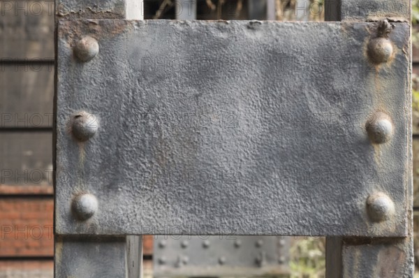 Close-up of a weathered gray metal plate attached to a larger metal structure with rivets, showing