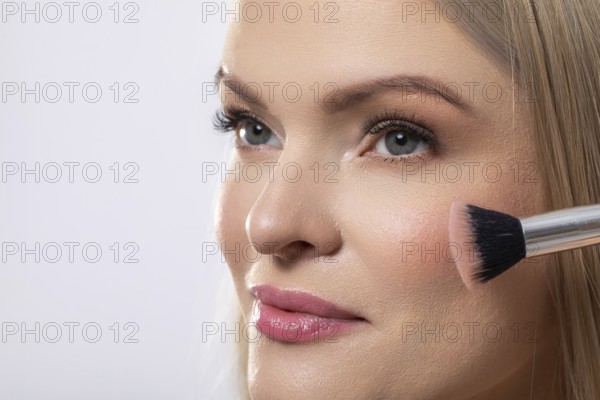 This is a professional makeup application showcasing a model skillfully utilizing a blush brush for
