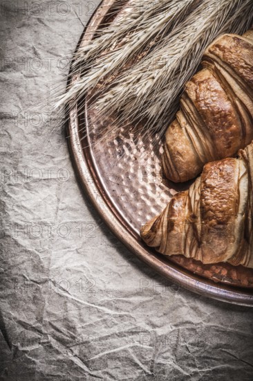 Golden wheat rye ears fresh croissants copper tray on wrapping paper