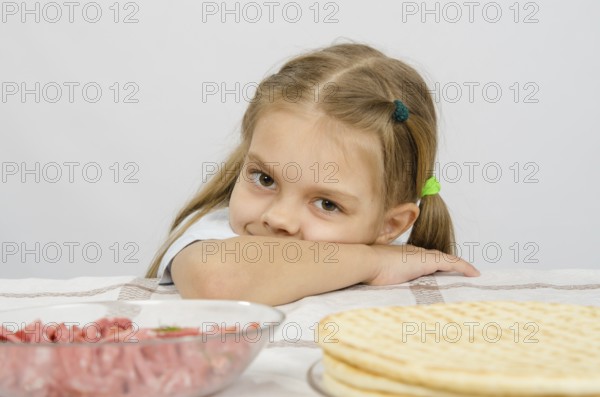 Little girl sitting at a table with his head on his hand with a smile and looking at the food in