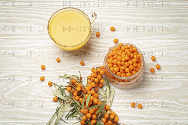 Sea buckthorn healthy hot tea in transparent glass cup, ripe berries in glass jar and branches with