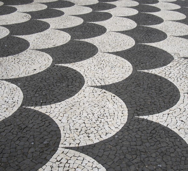 Traditional portugal black and white fish scale pattern tiled cobblestone sidewalk in funchal