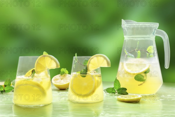 Lemonade with mint on a green background. Lemon water drink with ice. Two glasses and a pitcher.