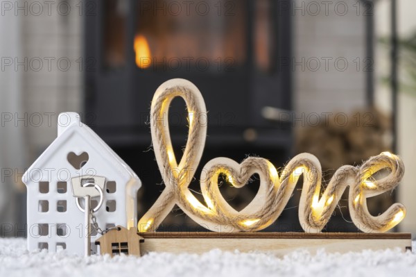 Key to house with keychain against background of fireplace stove with fire and firewood in