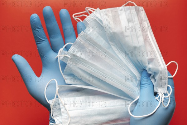 Doctor holds respiratory surgical face mask in hands blue medical gloves on red background.