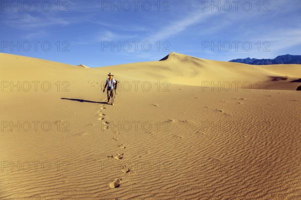 Woman with a camera and a tripod goes among the dunes. USA. Mesquite Flat Sand Dunes, Death Valley,