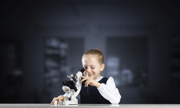 Little girl scientist looking through microscope in classroom at biology lesson. Research and