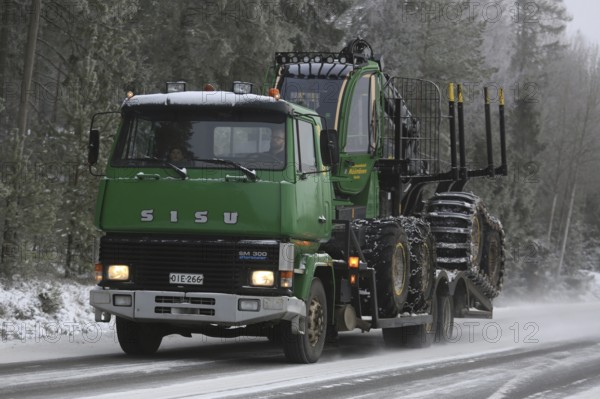 SALO, FINLAND, JANUARY 8, 2017: Green SISU SM300 truck transports a John Deere Forestry forwarder